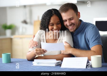 Heureux couple interracial vérifiant la réception dans la cuisine à la maison Banque D'Images