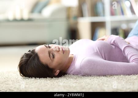 Femme distraite allongée sur le sol regardant loin dans le salon à la maison Banque D'Images