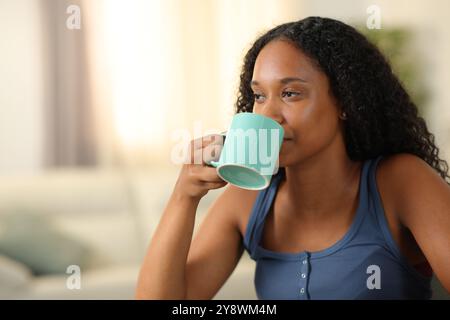 Femme noire sérieuse buvant du café ou du thé assis à la maison Banque D'Images