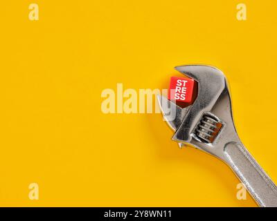 Clé réglable serrant un cube rouge avec le mot stress sur un fond jaune, image conceptuelle de la gestion du stress. Banque D'Images