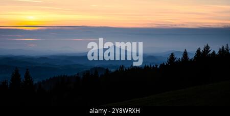 Une silhouette sereine de terrain vallonné se déploie alors que le soleil se couche derrière la montagne Ralsko en Tchéquie. Le paysage présente des couches de montagnes et de forêts dans la lumière tranquille du soir. Banque D'Images