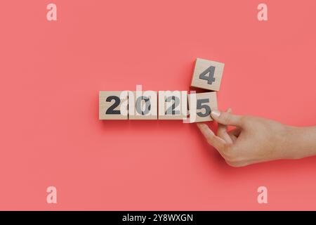 Changer à la main des cubes en bois de 2024 à 2025 sur fond rouge. Transition vers la nouvelle année. rendu 3d. Banque D'Images