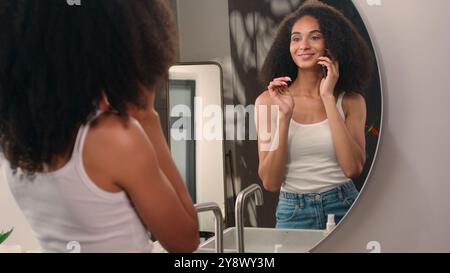 Femme afro-américaine marchant viennent dans la salle de bain heureux parler appel de téléphone mobile avec des amis fille ethnique regardant miroir réflexion vérifier coiffure Banque D'Images