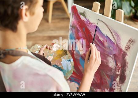 Une jeune femme dans un cadre détendu se concentre sur la peinture avec des couleurs vibrantes à la maison, exprimant sa créativité. Banque D'Images