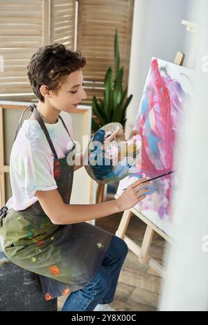 Une jeune femme aux cheveux courts aime peindre sur une toile à la maison, exprimant sa passion artistique. Banque D'Images