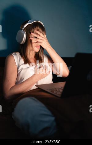 Femme regardant un film d'horreur effrayant sur ordinateur portable couché sur le lit tard dans la nuit, elle est effrayée couvrant le visage. Vue verticale Banque D'Images