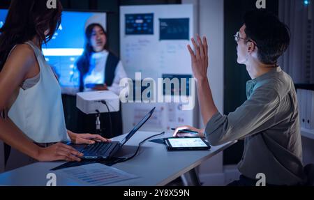 finan poser une question lorsque le chef examine les données pendant une réunion nocturne, les projections financières et les rapports numériques affichés à l'écran Banque D'Images