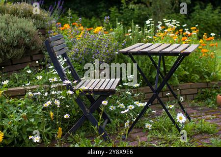 jardin sauvage - spirale d'herbes dans le jardin avec des herbes fraîches et des fleurs, table et chaise Banque D'Images