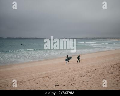 Lonely surfers on the beach in spring on a cloudy day at the seaside of peniche Portugal coast Stock Photo