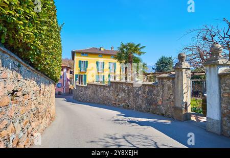 La rue courbe via principale, bordée de clôtures en pierre, cachant de beaux jardins verdoyants et des maisons historiques, Carona, Tessin, Suisse Banque D'Images