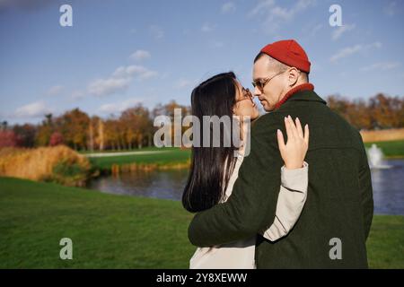 Un couple aimant profite d'une étreinte chaleureuse, entouré d'un feuillage d'automne vibrant près d'un lac tranquille. Banque D'Images