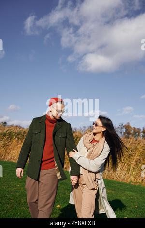 Un couple marche main dans la main, partageant rire et chaleur tout en profitant d’une belle journée d’automne. Banque D'Images