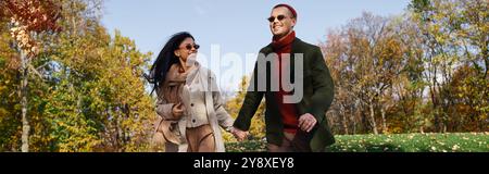 Un couple aimant marche main dans la main à travers les arbres d'automne vibrants, appréciant les uns les autres compagnie. Banque D'Images