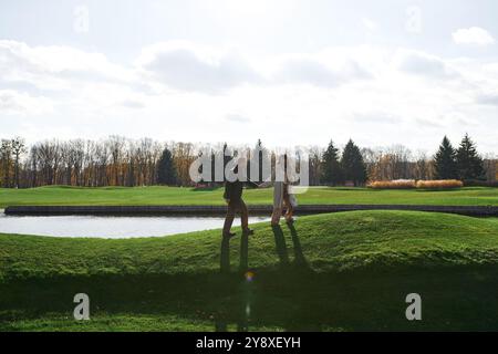 Un couple profite d'une promenade romantique main dans la main sur une journée d'automne fraîche au bord du lac tranquille. Banque D'Images