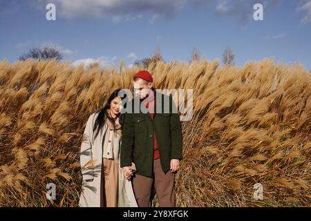 Enveloppé de chaleur et d'affection, un couple profite de leur promenade automnale à travers de hautes herbes dorées. Banque D'Images