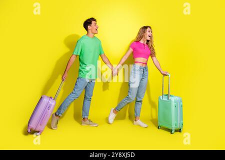 Photo pleine grandeur de deux jeunes gentils tiennent la main valise vide espace isolé sur fond de couleur jaune vif Banque D'Images