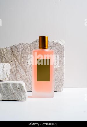 Un élégant flacon de parfum de pulvérisation de couleur pêche mis en valeur sur un fond de pierre blanche propre. Ce design minimaliste met en valeur la teinte douce et sophi Banque D'Images