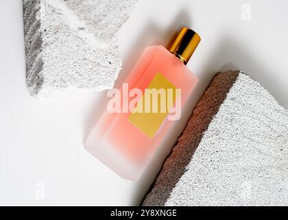 Un élégant flacon de parfum de pulvérisation de couleur pêche mis en valeur sur un fond de pierre blanche propre. Ce design minimaliste met en valeur la teinte douce et sophi Banque D'Images