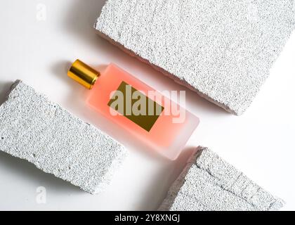 Un élégant flacon de parfum de pulvérisation de couleur pêche mis en valeur sur un fond de pierre blanche propre. Ce design minimaliste met en valeur la teinte douce et sophi Banque D'Images