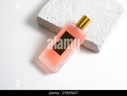 Un élégant flacon de parfum de pulvérisation de couleur pêche mis en valeur sur un fond de pierre blanche propre. Ce design minimaliste met en valeur la teinte douce et sophi Banque D'Images