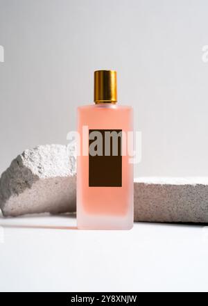 Un élégant flacon de parfum de pulvérisation de couleur pêche mis en valeur sur un fond de pierre blanche propre. Ce design minimaliste met en valeur la teinte douce et sophi Banque D'Images