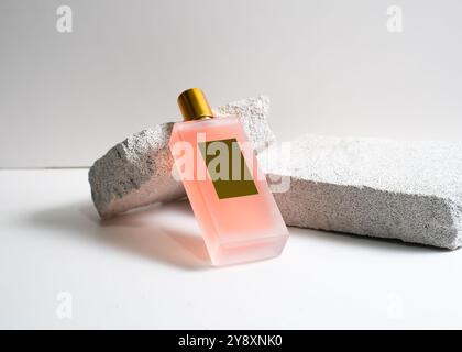 Un élégant flacon de parfum de pulvérisation de couleur pêche mis en valeur sur un fond de pierre blanche propre. Ce design minimaliste met en valeur la teinte douce et sophi Banque D'Images