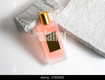 Un élégant flacon de parfum de pulvérisation de couleur pêche mis en valeur sur un fond de pierre blanche propre. Ce design minimaliste met en valeur la teinte douce et sophi Banque D'Images