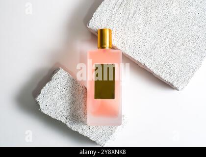 Un élégant flacon de parfum de pulvérisation de couleur pêche mis en valeur sur un fond de pierre blanche propre. Ce design minimaliste met en valeur la teinte douce et sophi Banque D'Images