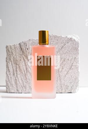 Un élégant flacon de parfum de pulvérisation de couleur pêche mis en valeur sur un fond de pierre blanche propre. Ce design minimaliste met en valeur la teinte douce et sophi Banque D'Images