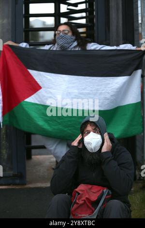 Blackburn, Angleterre, Royaume-Uni. 7 octobre 2024. Un cri de protestant couvre ses oreilles alors qu'un policier lit les règlements de l'article 14 pendant la manifestation. Les manifestants bloquent les quatre portes et refusent l'accès au personnel de BAE Systems à Samlesbury. Cette manifestation marque le premier anniversaire du début de la guerre Gaza/Israël qui a fait plus de 41 000 morts parmi les civils. Les manifestants accusent BAE Systems d'être complice du génocide de Gaza en produisant les avions de chasse F-35 dans leurs installations de Samlesbury. Crédit : ZUMA Press, Inc/Alamy Live News Banque D'Images