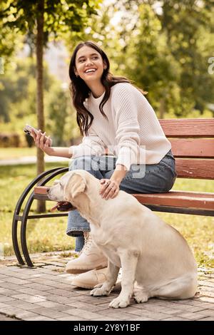 Une jeune femme en tenue d'automne confortable se détend sur un banc, souriant comme elle caresse son chien. Banque D'Images