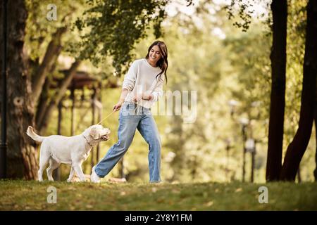 Une jeune femme joyeuse promène son chien dans un parc pittoresque entouré de feuilles d'automne colorées. Banque D'Images