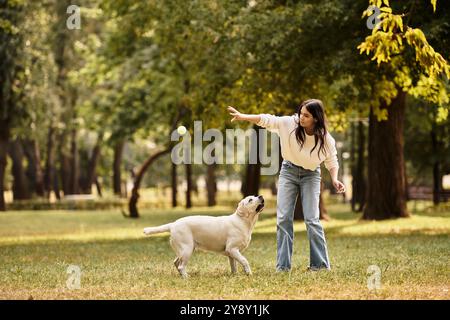 Une jeune femme dans des vêtements d'automne confortables lance joyeusement une balle pour son chien dans un parc. Banque D'Images