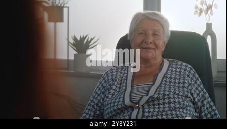 Femme âgée assise dans la chaise écoutant les conseils du psychologue ou du psychothérapeute, recevant un soutien psychologique pendant la consultation. Le patient ressent des émotions positives et rit. Gros plan. Portrait. Banque D'Images