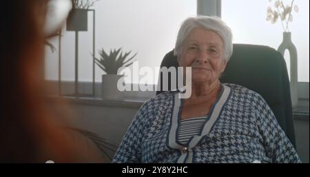 Femme âgée assise dans la chaise écoutant les conseils du psychologue ou du psychothérapeute, recevant un soutien psychologique pendant la consultation. Le patient ressent des émotions positives et rit. Gros plan. Portrait. Banque D'Images