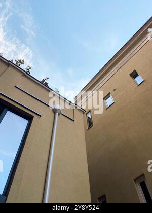 Regardant vers le haut à l'intersection de deux bâtiments beiges modernes contre un ciel bleu vif. Scène urbaine minimaliste, soulignant le contraste entre Banque D'Images