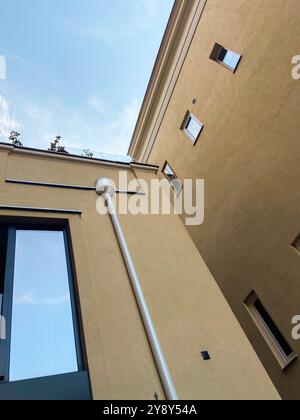 Regardant vers le haut à l'intersection de deux bâtiments beiges modernes contre un ciel bleu vif. Scène urbaine minimaliste, soulignant le contraste entre Banque D'Images