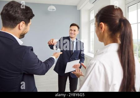 Un agent immobilier professionnel donne la clé de la maison à un jeune couple de clients. Banque D'Images