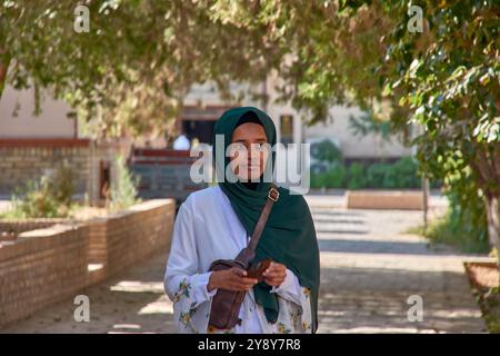 Khiva, Ouzbékistan ; septembre, 21,2024:une femme musulmane à la peau foncée, portant un voile vert vif, marchant dans les rues historiques de Khiva, Ouzbékistan Banque D'Images