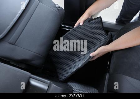 Homme prenant tapis de voiture en caoutchouc gris de l'auto, gros plan Banque D'Images