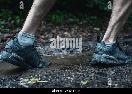 Jambes d'un coureur masculin athlétique non reconnu courir sur un sentier boueux forestier en saison d'automne Banque D'Images