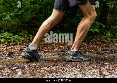 Jambes d'un coureur masculin athlétique non reconnu courir sur un sentier boueux forestier en saison d'automne Banque D'Images