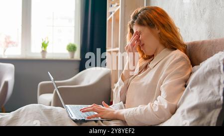 Femme freelance dans le lit du matin ordinateur portable de travail sentir mal de tête migraine symptôme de gueule de bois caucasien fille malade étudiant à distance de l'ordinateur de navigation à la maison Banque D'Images