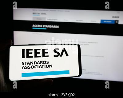 Personne tenant le téléphone portable avec le logo de l'IEEE Standards Association sur l'écran en face de la page Web. Concentrez-vous sur l'affichage du téléphone. Banque D'Images