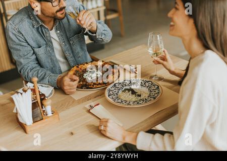 Deux personnes savourent leurs boissons à une table en bois, immergées dans une ambiance de restaurant détendue, tout en étant profondément dans la conversation et les rires. Banque D'Images