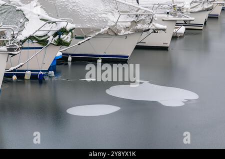 Les bateaux se trouvent tranquillement nichés dans un port enneigé, entourés d'un paysage gelé qui brille dans la douce lumière du matin. Banque D'Images