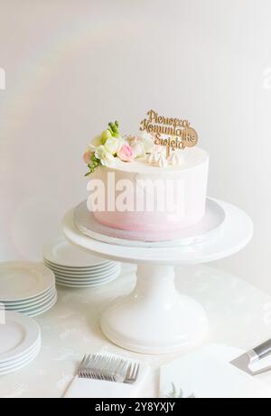 Elégant gâteau de première communion avec décoration florale et topper en bois pour 'Pierwsza Komunia Święta' (première communion en polonais) Banque D'Images