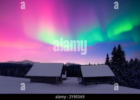 Paysage hivernal de fées avec des cabines en bois dans les montagnes enneigées et aurores boréales dans le ciel nocturne. Vacances de Noël et vacances d'hiver concept Banque D'Images