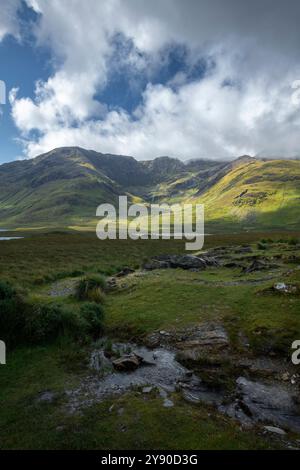 Jeu de lumière et d'ombre à travers l'herbe verte luxuriante des pentes de montagne à Doo Lough Valley, Glencullin Mountain, comté de Mayo, Irlande Banque D'Images