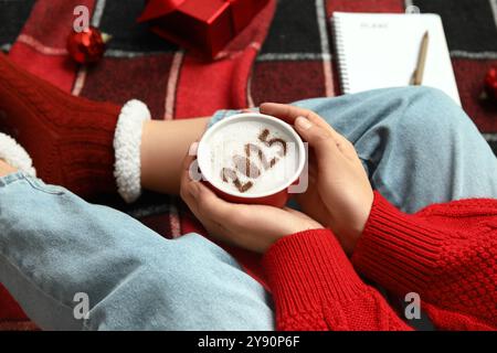 Femme tenant une tasse de café avec la figure 2025 sur le plaid à carreaux rouge, gros plan Banque D'Images